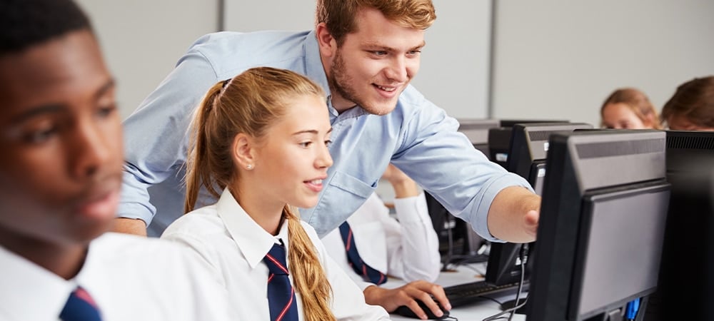 Teacher helping secondary pupil on computer